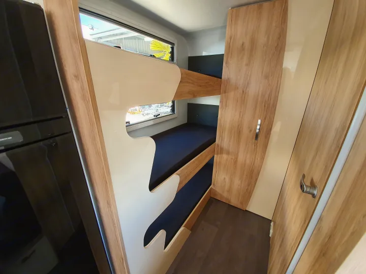 Inside an RV rental: modern bunk beds with cream accents, built-in fridge, and wood wardrobe maximize space.. Avan Aspire 617 Family 2021
