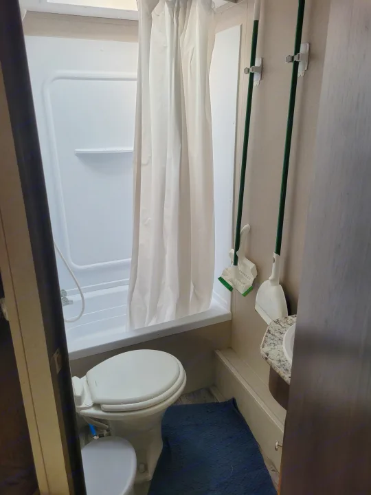 Compact RV rental bathroom with white shower, toilet, and wall-mounted cleaning tools on the right.. Keystone Hideout 2019