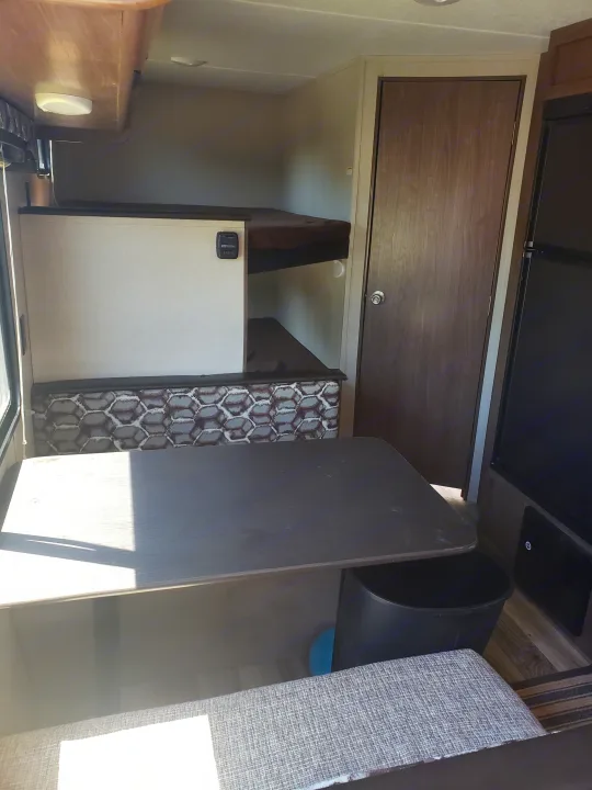 RV rental interior showing a dinette with a dark table, geometric patterned bench, bunk beds, and a brown wooden door.. Keystone Hideout 2019