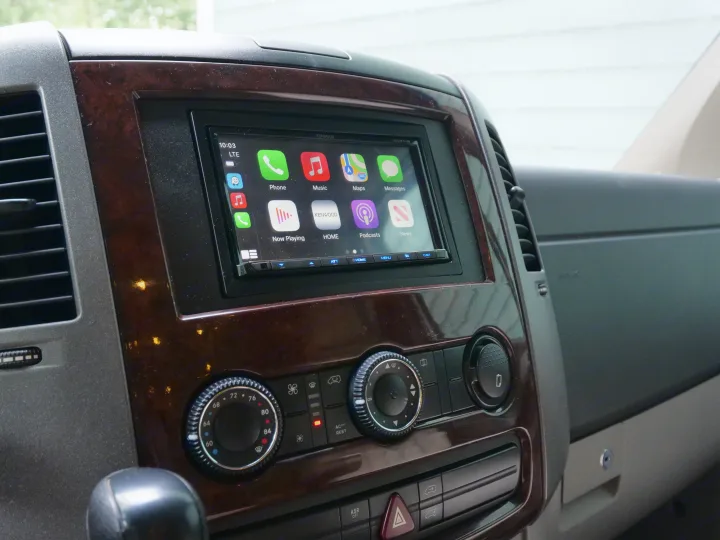 RV rental dashboard: Kenwood Apple CarPlay stereo displaying apps, flanked by air vents, with climate controls below.. Airstream Interstate 2010