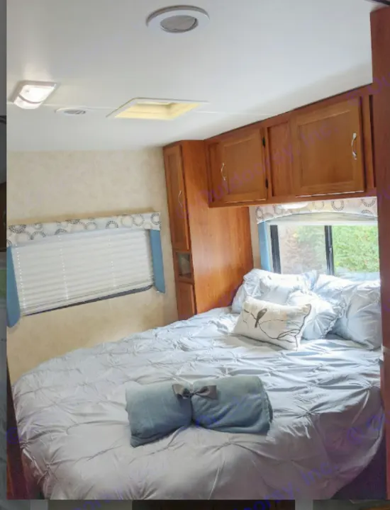 Comfortable RV rental bedroom with blue bedding, window, and wood cabinets. Ideal for travel.. Forest River Coachmen Freelander 2011