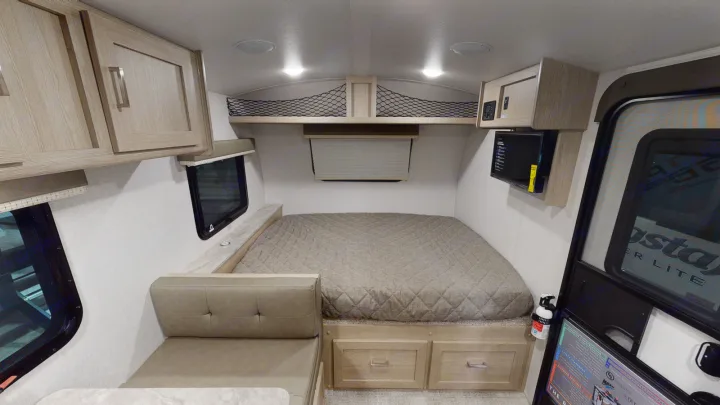 Compact RV rental interior featuring a cozy bed, small dinette, overhead storage, and microwave.. Forest River Other 2021