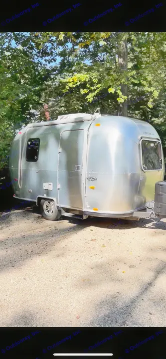 Experience nature with this stunning silver Airstream travel trailer, ideal for your next rv rental adventure, parked under sun-dappled trees.. Airstream Safari 2008