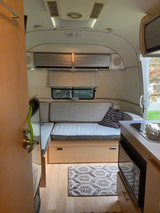Inside a modern RV rental: comfortable grey seating, kitchen area with sink & microwave, and overhead storage.. Airstream Safari 2008