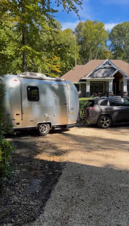 This Airstream RV rental is hitched to an SUV on a gravel driveway, poised for a memorable road trip adventure.. Airstream Safari 2008