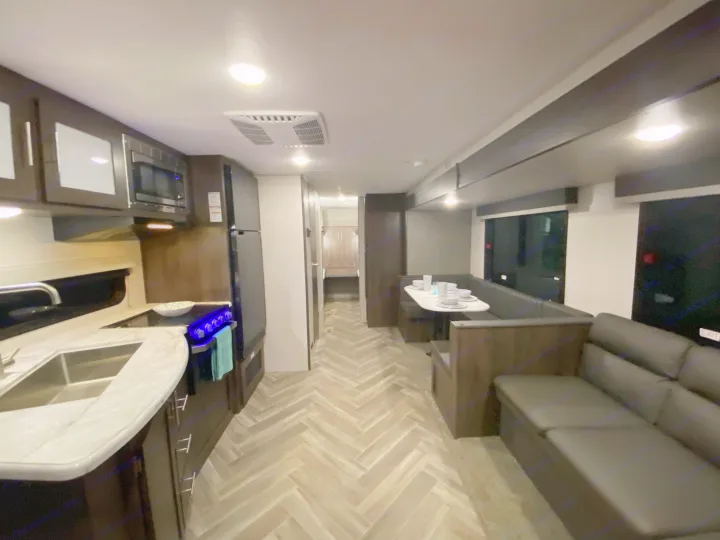 Spacious rv rental interior: modern kitchen, dining booth, cozy sofa, and stylish herringbone floor.. K-Z Manufacturing Sportsmen 2021