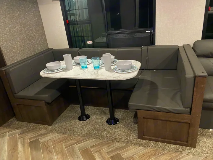 Cozy RV rental dinette with U-shaped seating, marble-look table set with dishes. Perfect for meals on the go.. K-Z Manufacturing Sportsmen 2021