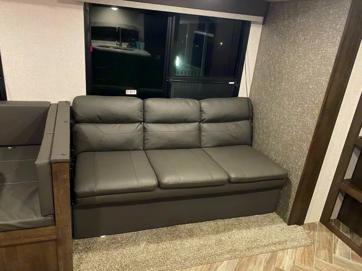 Comfortable RV rental living space featuring a dark grey sofa, large window, and modern interior design elements.. K-Z Manufacturing Sportsmen 2021
