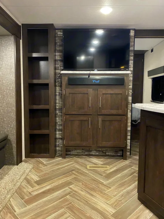 Modern RV rental living area with entertainment center, TV, soundbar, storage, and stylish herringbone floor.. K-Z Manufacturing Sportsmen 2021