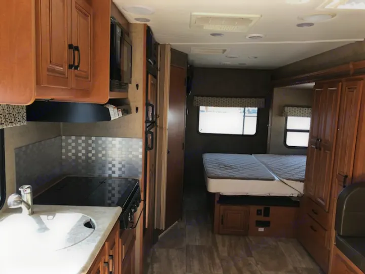 RV rental interior shows a compact kitchen with stove and sink, plus a cozy bedroom with twin beds.. Forest River Sunseeker 2017