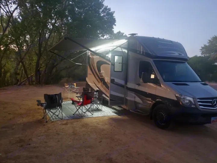 Night view of an RV rental campsite. A motorhome with an extended awning illuminates camping chairs and a table for outdoor leisure.. Forest River Sunseeker 2017