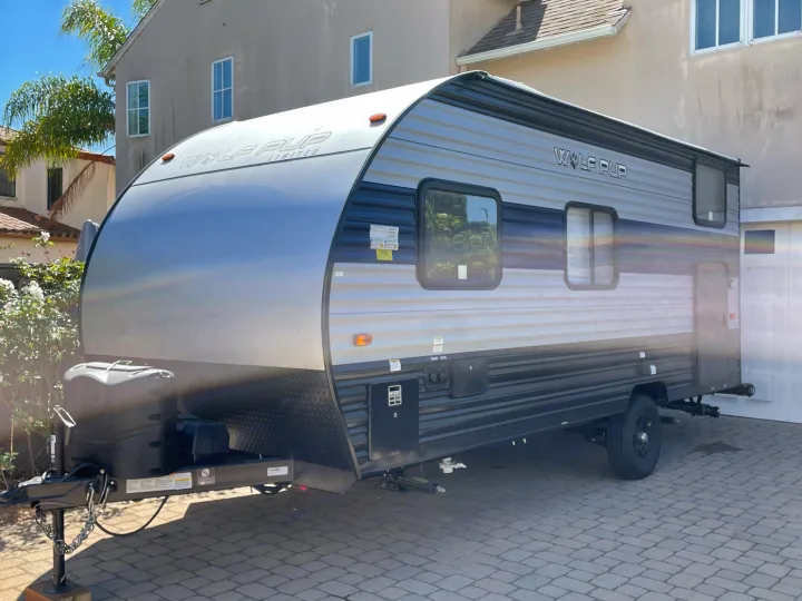 A modern, silver and black Wolf Pup travel trailer, ideal for an RV rental. Parked on a paved driveway in sunlight.. Forest River Cherokee Wolf Pup 2022