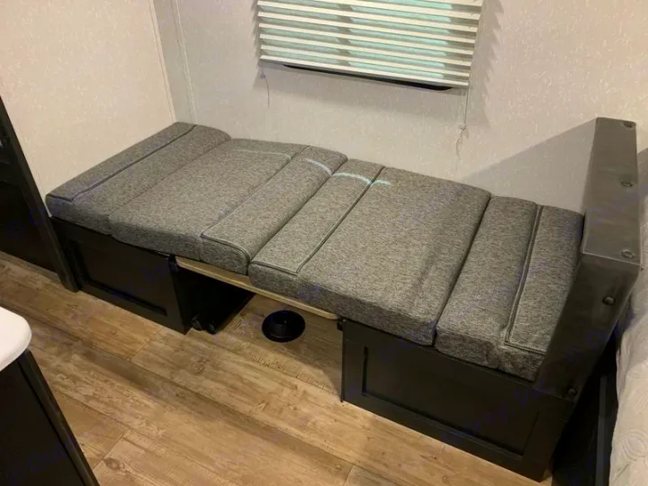 RV rental's convertible dinette bench with grey cushions, extended for flexible seating and sleeping space.. Forest River Cherokee Wolf Pup 2022