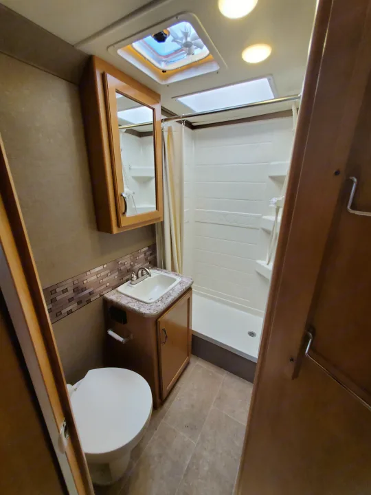 Clean RV rental bathroom featuring a toilet, sink vanity, and standing shower with curtain. Brightly lit with skylights.. Other Other 2017