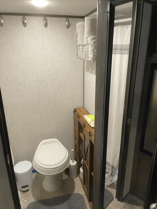 Inside an RV rental: a compact bathroom with toilet, shower, rustic cabinet, and towel storage.. Coleman Other 2022