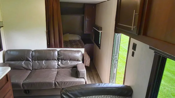 RV rental interior: Comfortable brown sofa, compact bed area with curtains, and bright outdoor view through the doorway.. Jayco Jay Flight 2019