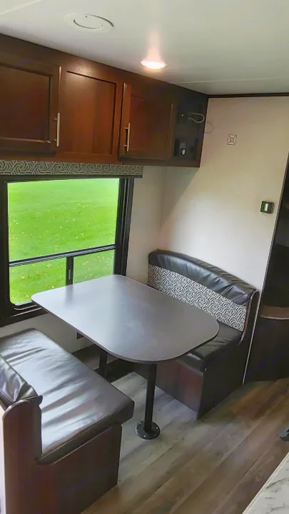 Cozy RV rental dinette featuring bench seating, a table, and a window overlooking greenery. Ideal for road trips.. Jayco Jay Flight 2019