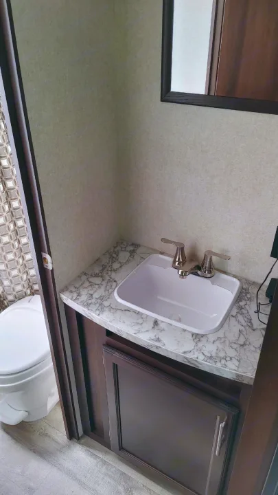 An RV rental bathroom with a white sink, marble countertop, dark wood vanity, and toilet visible. Light beige walls.. Jayco Jay Flight 2019