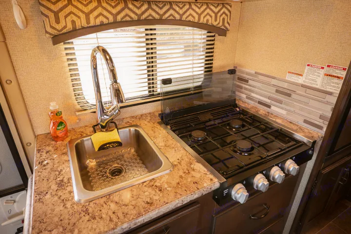 Inside an RV rental: a modern kitchenette featuring a sink with a curved faucet, dish soap, and a multi-burner gas stove.. Thor Motor Coach Chateau 2019