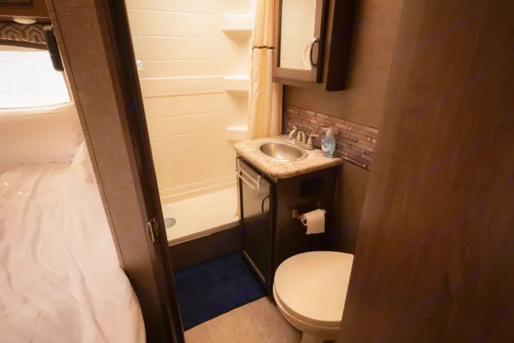 RV rental interior featuring a compact bathroom with toilet, sink, and shower, adjacent to a bright sleeping area.. Thor Motor Coach Chateau 2019