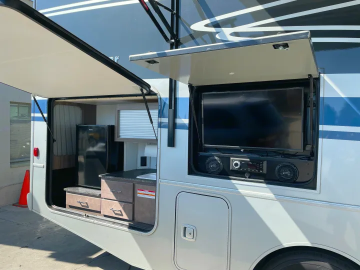 This rv rental boasts an outdoor kitchen with a fridge and sink, plus an entertainment system with a TV and speakers.. Winnebago Adventurer 2022