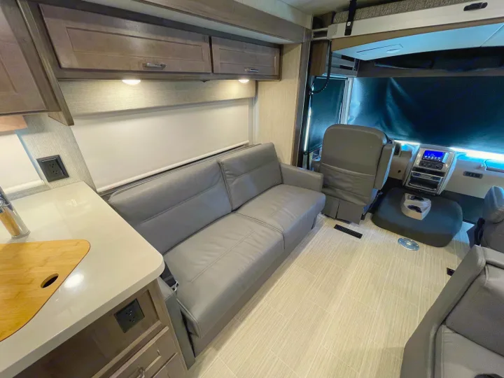 RV rental interior: living area with gray sofa, kitchen counter, and front cockpit. Perfect for travel comfort.. Winnebago Adventurer 2022