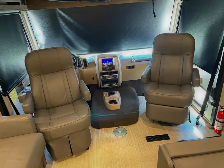 Inside an RV rental: view of the front cockpit with swiveling driver and passenger seats, dashboard controls, and privacy shades.. Winnebago Adventurer 2022