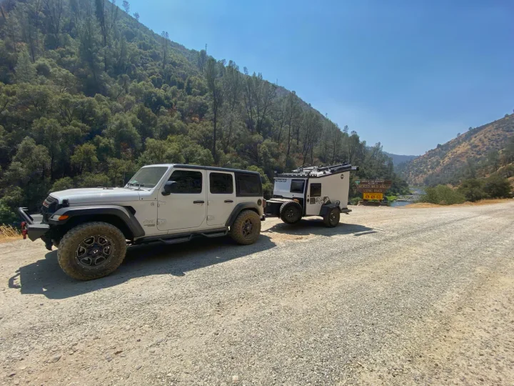 White Jeep and compact RV rental camper on a gravel road by the Merced Wild & Scenic River, perfect for off-road adventure.. TAXA Outdoors Tigermoth Camper 2021