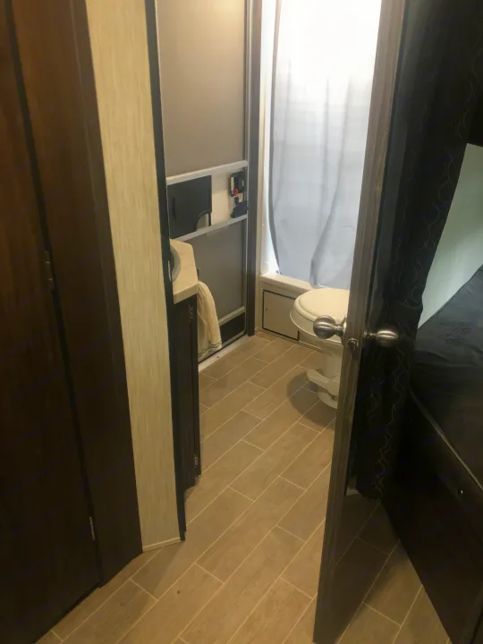 Inside an RV rental: view of a compact bathroom (toilet, sink, shower curtain) and adjacent bedroom, showing efficient use of space.. Forest River Cherokee Grey Wolf 2020