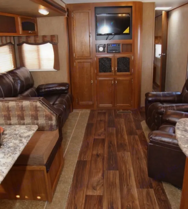 View of an RV rental's spacious living area, featuring brown leather seating, wood-look flooring, and a built-in entertainment center.. Forest River Avenger 28RKS 2015