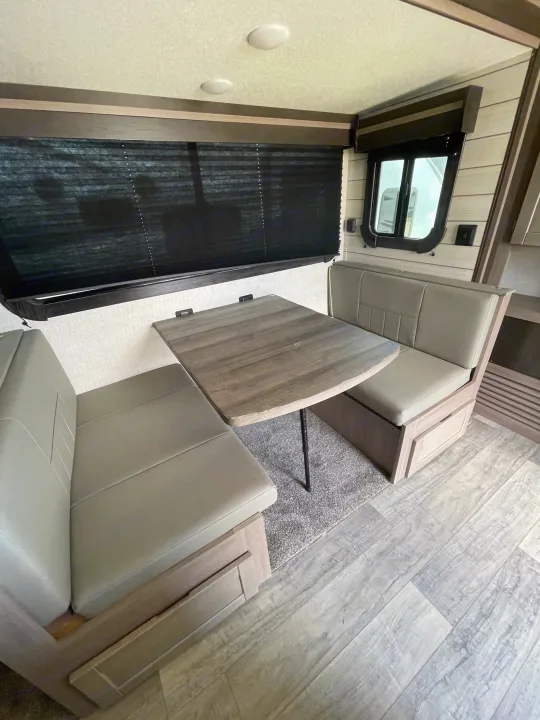 An RV rental interior features a cozy dinette with light-colored bench seating, a wooden table, and dark window blinds.. Crossroads RV Sunset Trail Super Lite 2021