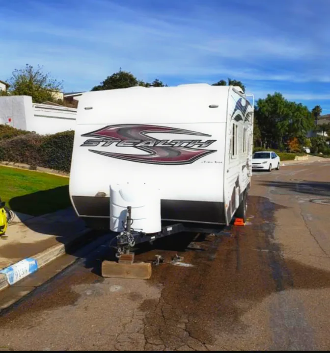 A white 'Stealth' travel trailer, likely an RV rental, is parked on a wet residential street, possibly being cleaned.. Forest River Stealth 2012