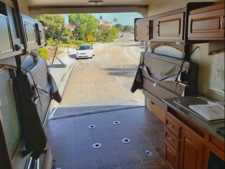 Inside an RV rental toy hauler with its rear ramp open, offering a street view. Features include fold-up beds & a kitchen.. Forest River Stealth 2012