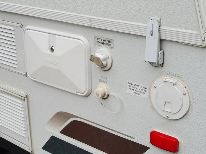 View of an RV rental's external utility panel, featuring shower, city water, sink drain, and 30-amp electric connections.. Starcraft Comet 2012