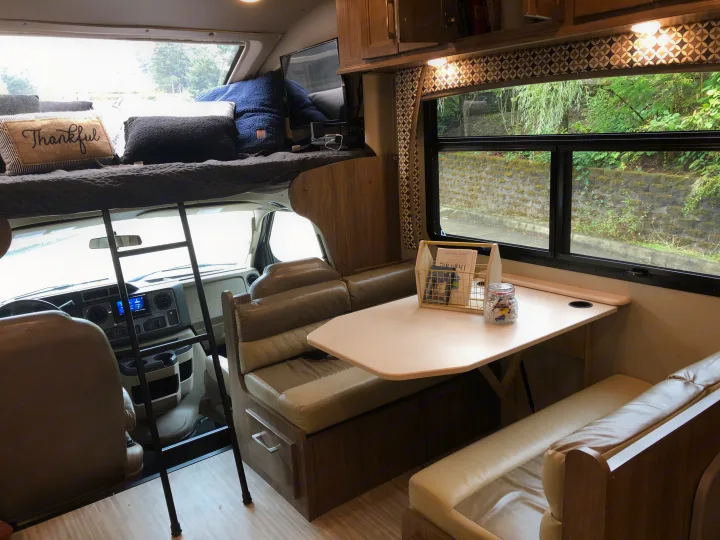 Cozy RV rental interior with dinette, bunk bed, and driver's cabin view. Perfect for travel adventures.. Jayco Greyhawk 2018
