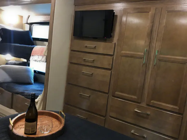 Cozy RV rental interior featuring bunk beds, a mounted TV, ample wardrobe & dresser storage, plus a small tray setup.. Jayco Greyhawk 2018