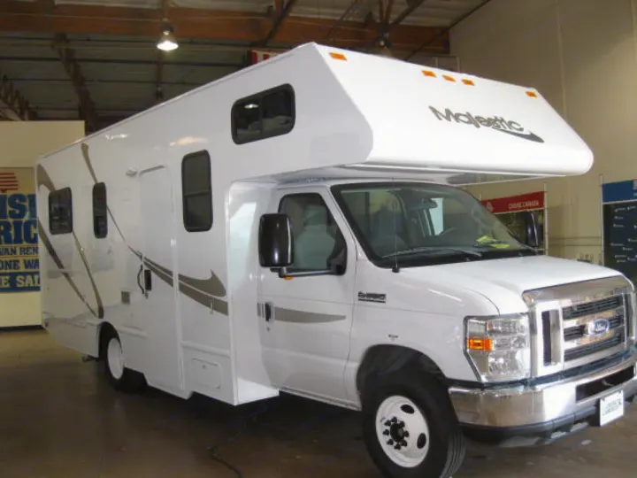 A white Majestic rv rental, a Class C Ford RV, shines brightly. It features brown graphic decals and a spacious over-cab area.. Thor Motor Coach Four Winds Majestic 2017