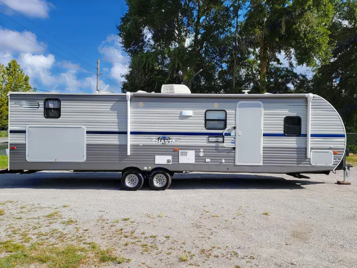 Grey travel trailer RV rental, parked on gravel. This spacious RV features horizontal stripes, multiple windows, and a main entrance door.. Other Other 2021