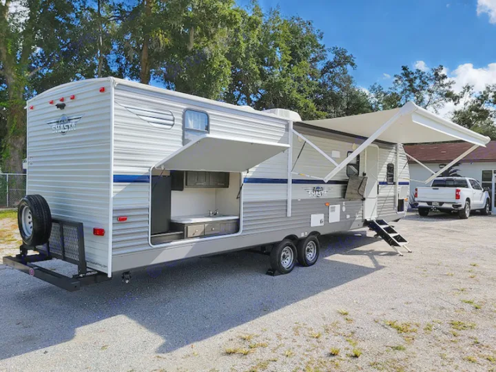 A Shasta RV rental travel trailer with an open outdoor kitchen, extended awning, and rear spare tire.. Other Other 2021