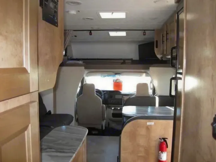 Spacious RV rental interior with front cab view, overhead bunk, and a practical kitchen counter.. Coachmen Leprechaun 2021
