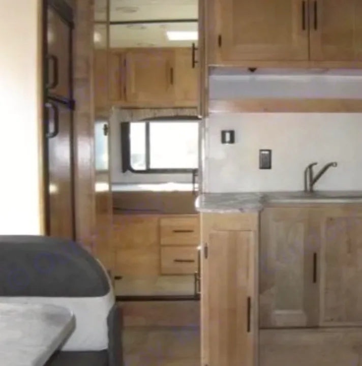 RV rental interior: Light wood kitchen with sink & upper/lower cabinets. Fridge, partial dining area, and hallway visible.. Coachmen Leprechaun 2021