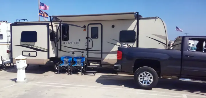 This RV rental travel trailer, a Rockwood Ultra Lite, is set up at a sunny campsite with a truck, awning, chairs, and flying flags.. Forest River Rockwood Ultra Lite 2018