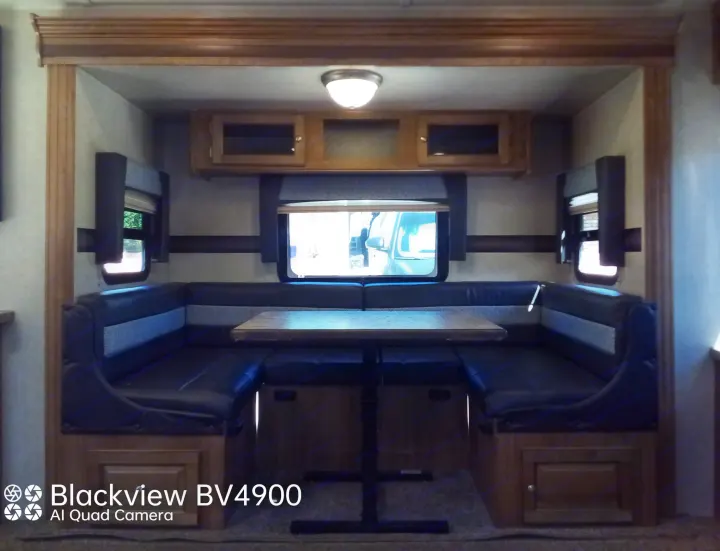 Inside a cozy RV rental: a U-shaped dinette with dark benches and wooden table, flanked by windows and overhead cabinets.. Forest River Rockwood Ultra Lite 2018