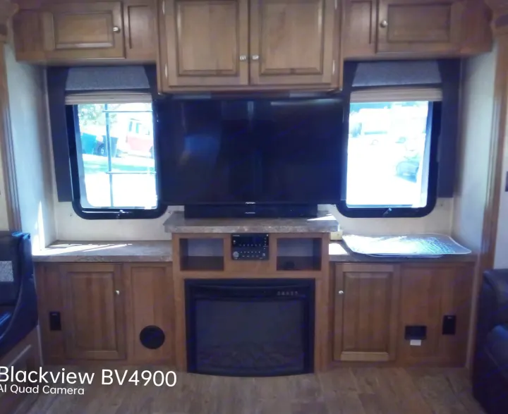Inside a cozy RV rental: living space with a large TV, fireplace, and wood cabinets flanking bright windows.. Forest River Rockwood Ultra Lite 2018