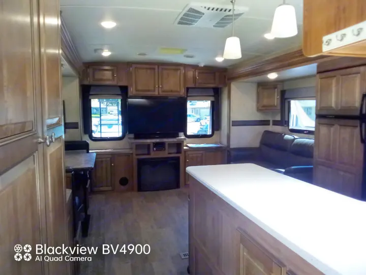 Spacious RV rental interior with a kitchen island, living area featuring a TV and fireplace, and a dining booth.. Forest River Rockwood Ultra Lite 2018