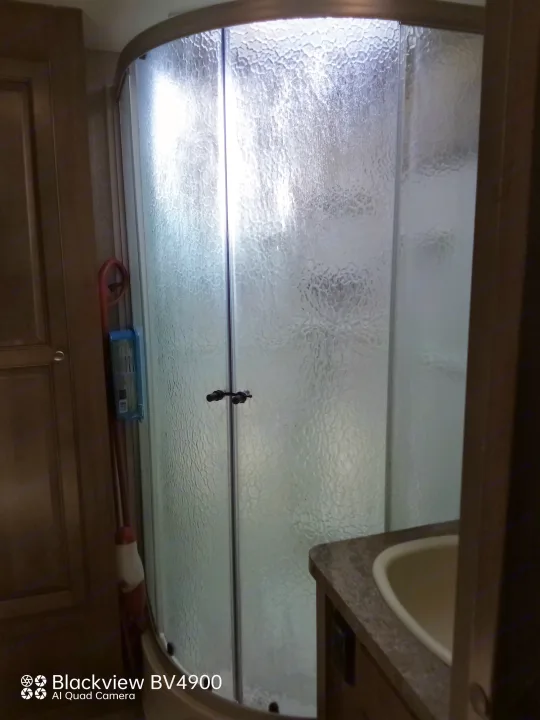 RV rental compact bathroom with curved frosted glass shower, sink vanity, and wooden cabinetry.. Forest River Rockwood Ultra Lite 2018