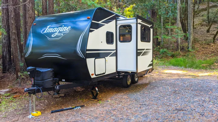 An RV rental is perfectly set up at a serene forest campsite, ready for adventure amidst towering trees.. Grand Design Imagine XLS 17MKE 2022
