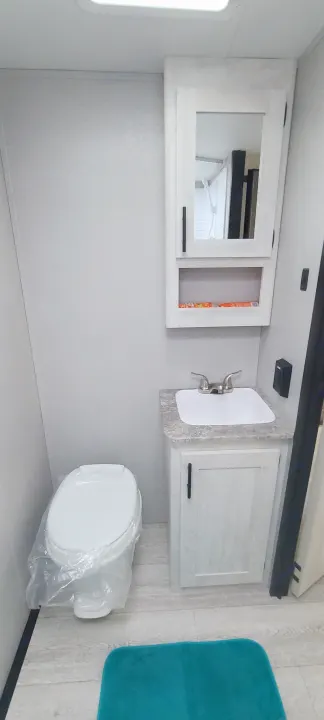 Compact RV rental bathroom featuring a wrapped toilet, sink vanity, and mirrored medicine cabinet.. Shasta BH18 2022