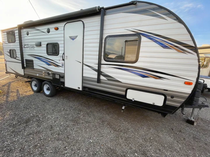 A sleek white and grey travel trailer with blue and gold accents, ideal for an rv rental, parked on gravel for your next adventure.. Forest River Cruise Lite 2019