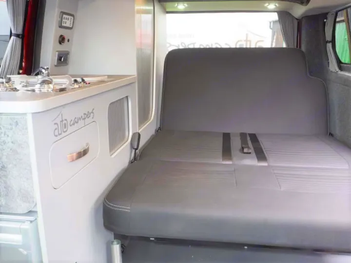 RV rental camper van interior showing a compact kitchen on the left and a gray upholstered bed/seat on the right.. Ford Transit Custom 2+2 berth Pop Top, Manual 2022